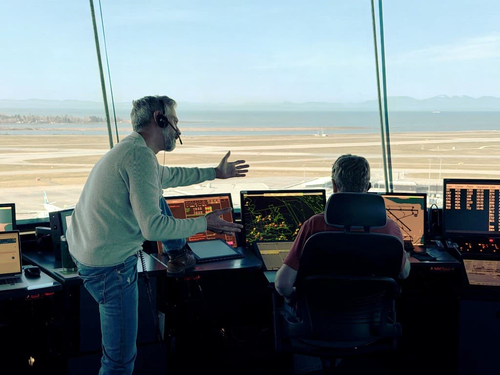 Air traffic controllers working in a tower cab with radar and flight displays, overlooking the airfield